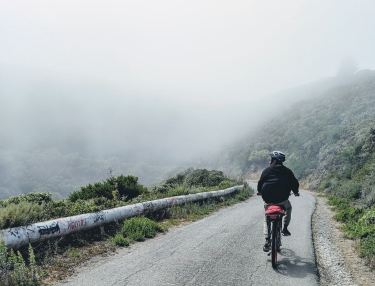 A cyclist on a small road in the hills, fading into mist in the distance.