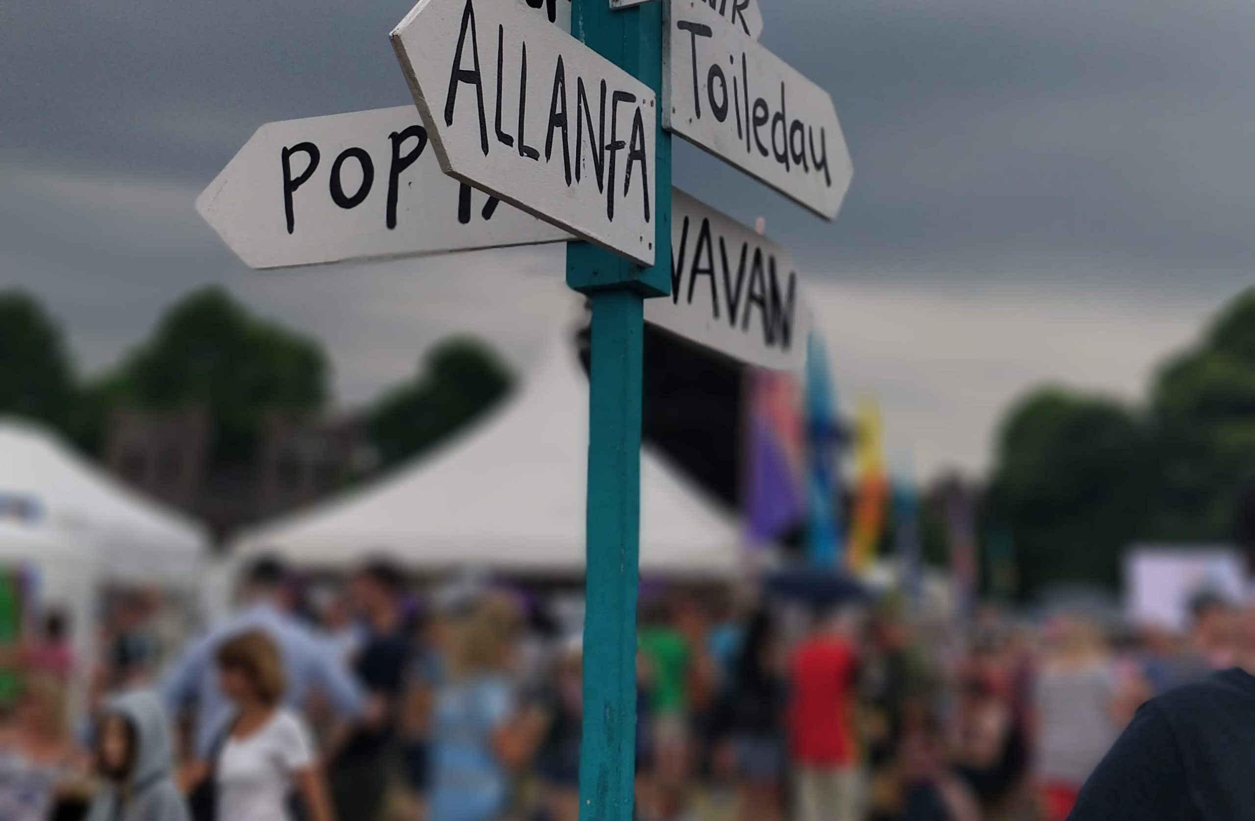 Picture of the bottom of a signpost at Tafwyl, with people and stands blurred in the background